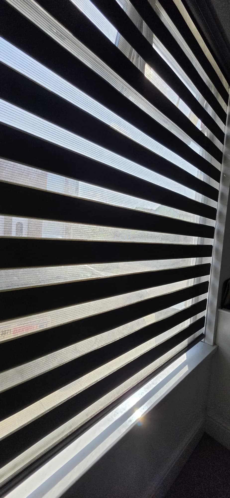 Close-up of a black day and night blind with light filtering between the bands