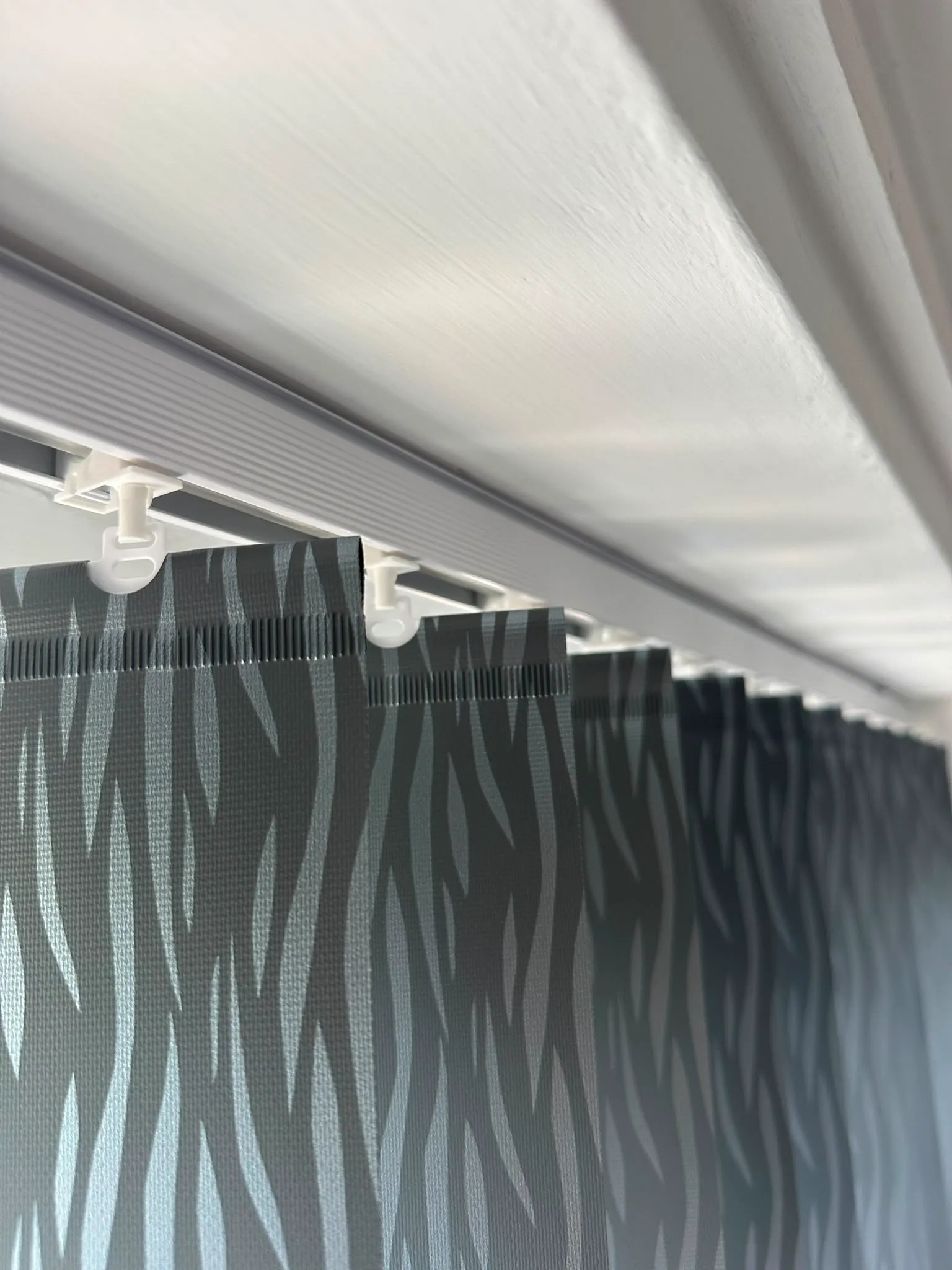 Close-up of grey patterned vertical blind louvres hanging from a white headrail track