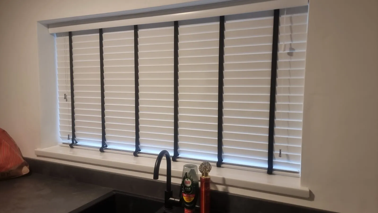 White-painted wooden Venetian blinds with tape ladders on a wide kitchen window