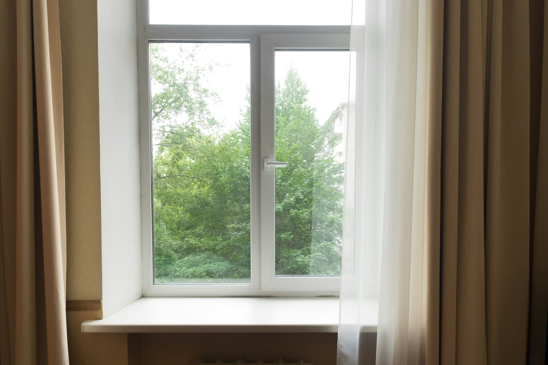 Bedroom window with sheer curtains and a radiator below
